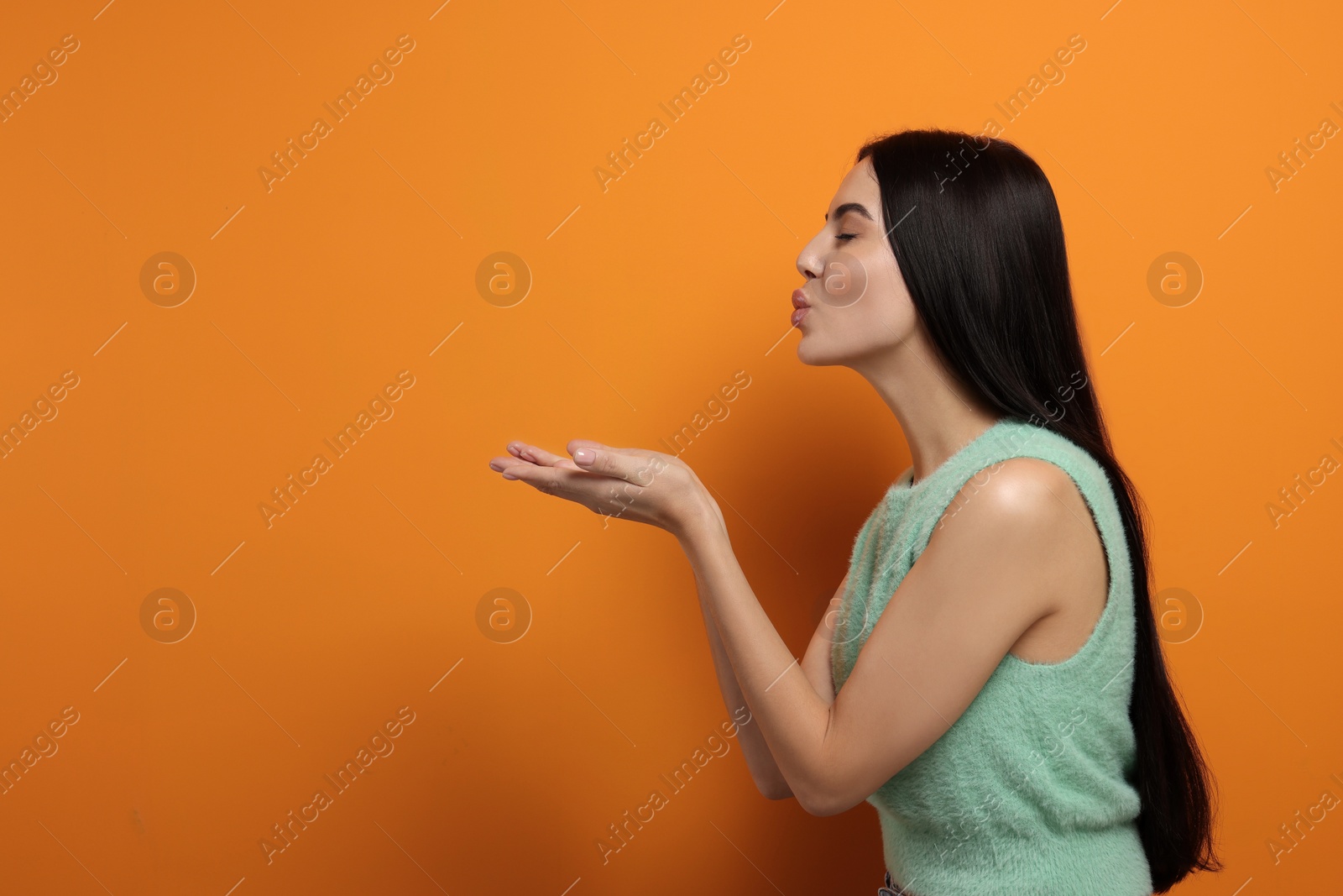 Photo of Beautiful young woman blowing kiss on orange background. Space for text