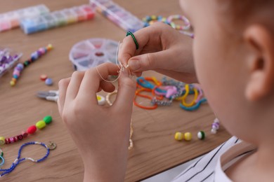 Photo of Little girl making beaded jewelry at table, closeup