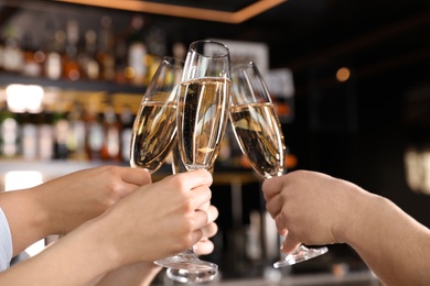 Photo of Friends clinking with glasses of champagne in bar, closeup