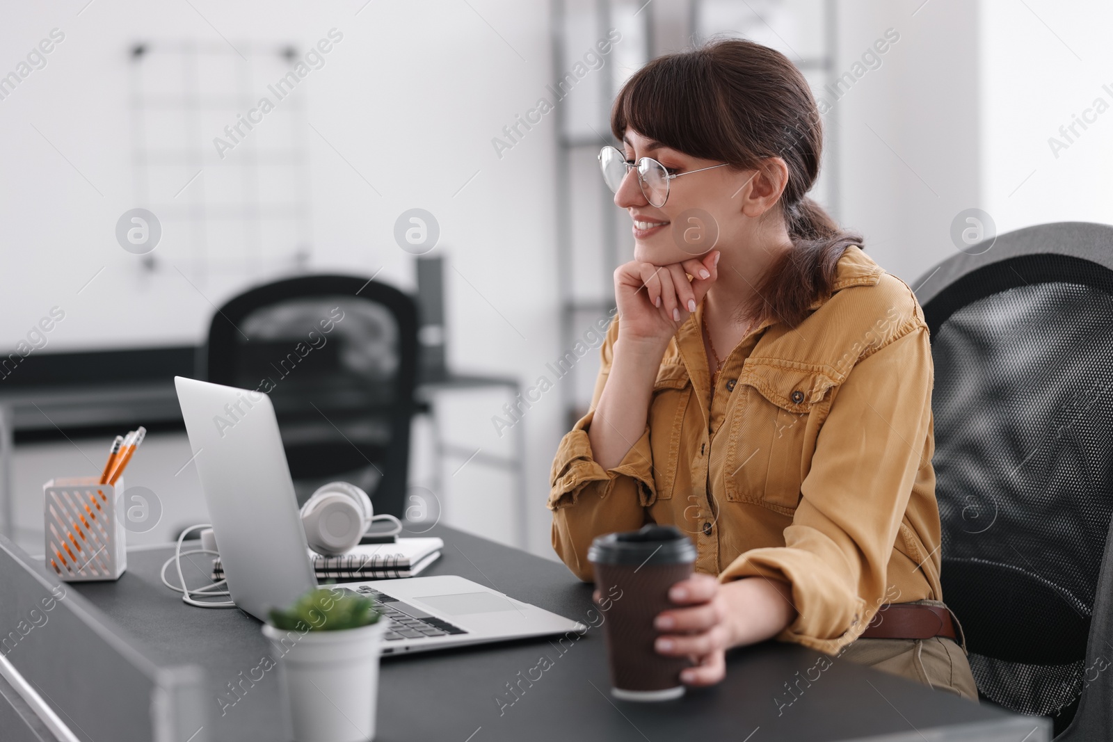 Photo of Woman with cup of coffee watching webinar at table in office