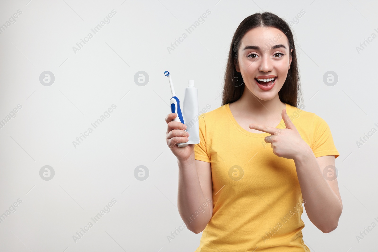 Photo of Happy young woman holding electric toothbrush and tube of toothpaste on white background, space for text