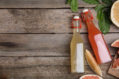 Photo of Glass bottles of different pomelo juices and fruits on wooden table, flat lay. Space for text