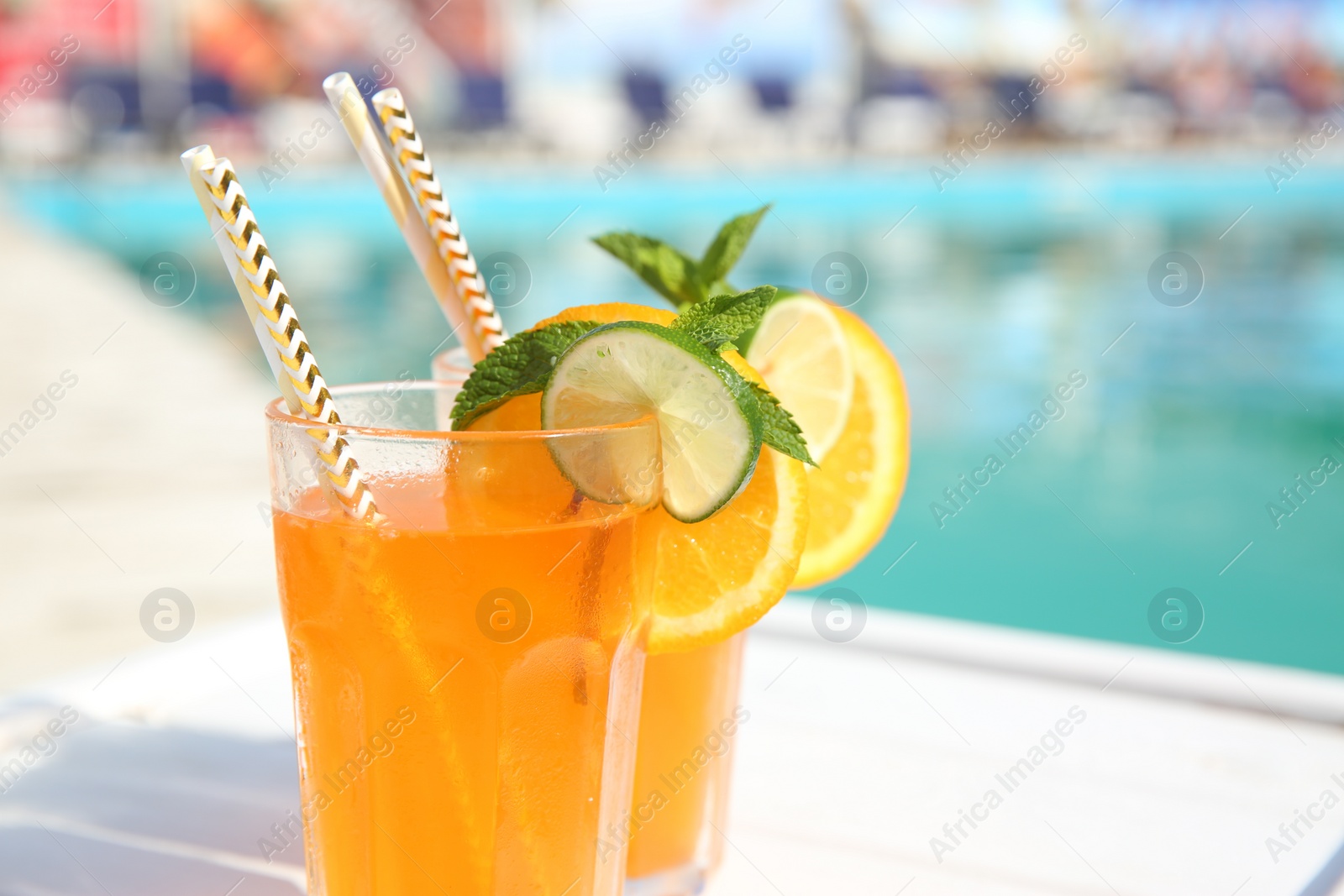 Photo of Refreshing cocktail in glasses near outdoor swimming pool on sunny day