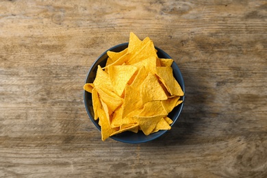 Tasty mexican nachos chips in color bowl on wooden table, top view