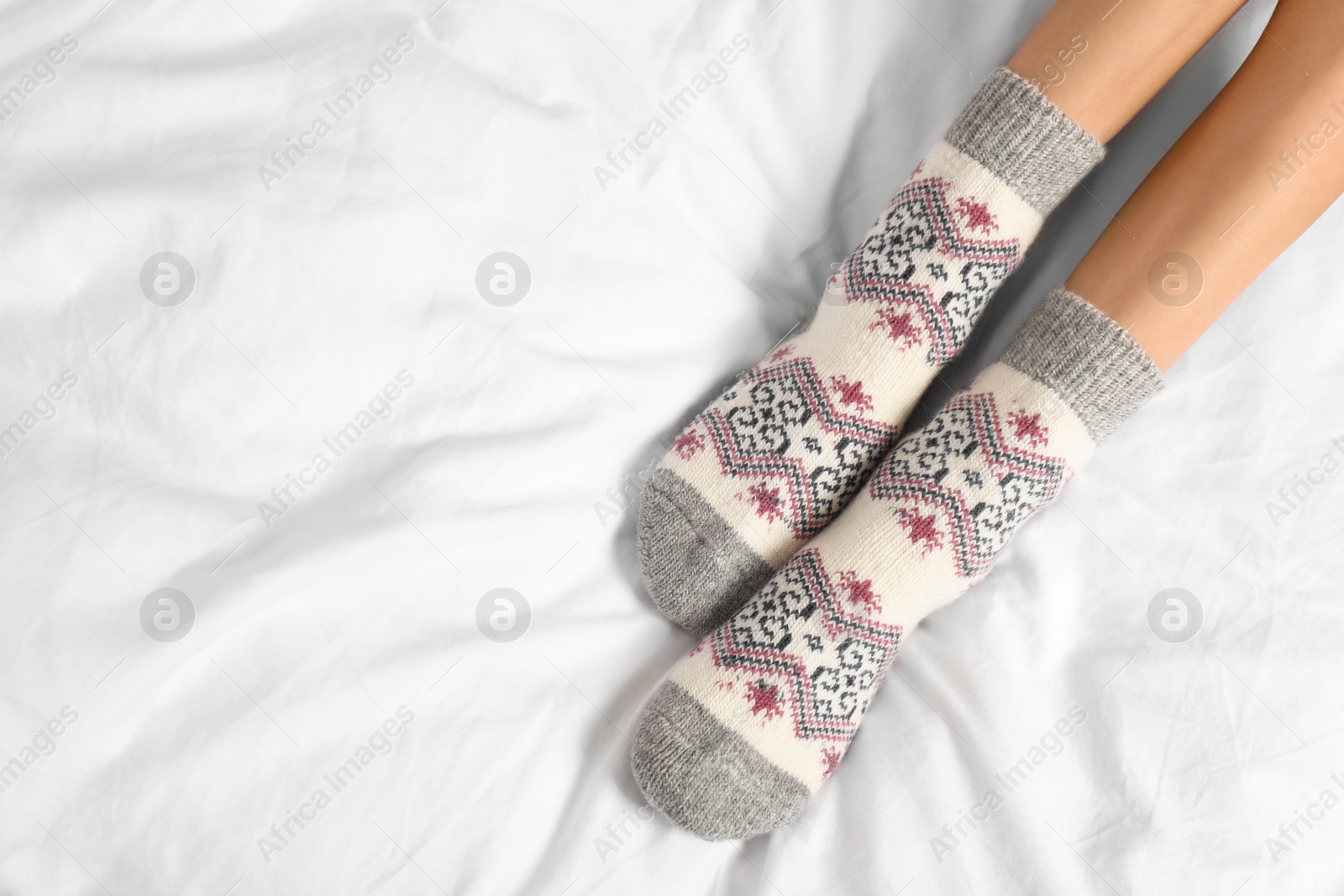 Photo of Woman wearing knitted socks on white fabric, top view with space for text. Warm clothes