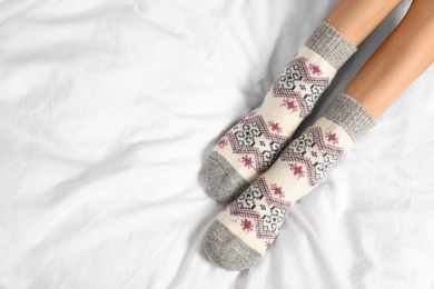 Woman wearing knitted socks on white fabric, top view with space for text. Warm clothes