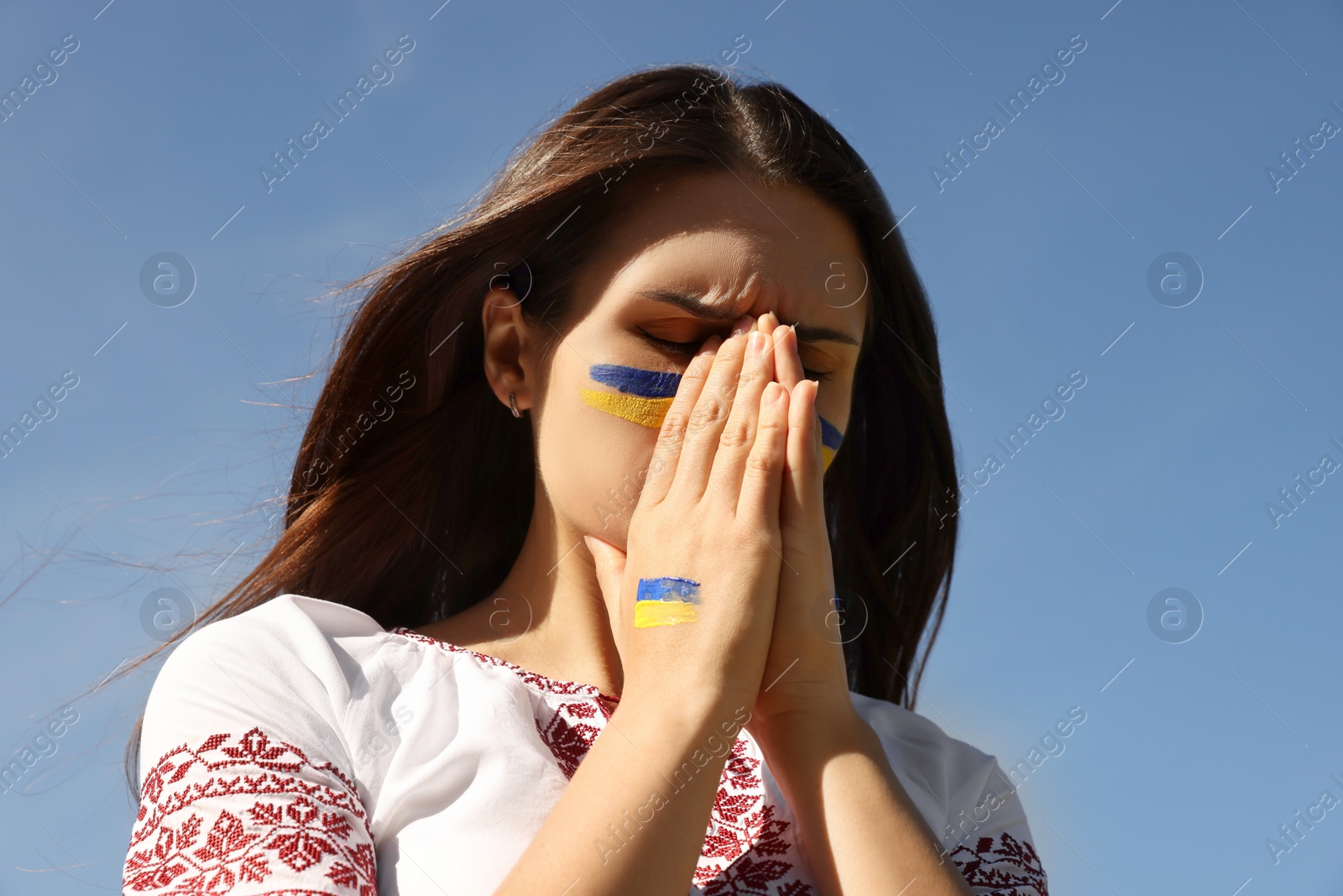 Photo of Young Ukrainian woman with clasped hands against blue sky