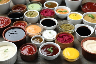 Photo of Many bowls with different sauces and herbs on wooden table
