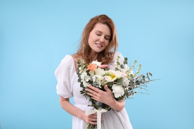 Beautiful woman with bouquet of flowers on light blue background