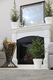 Photo of Little fir trees and Christmas decorations in room with fireplace. Stylish interior design