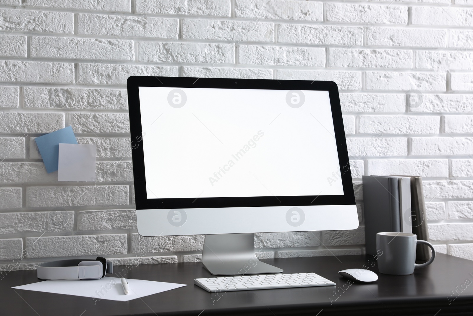 Photo of Comfortable workplace with modern computer on black table near white brick wall. Space for text