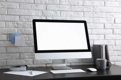 Comfortable workplace with modern computer on black table near white brick wall. Space for text