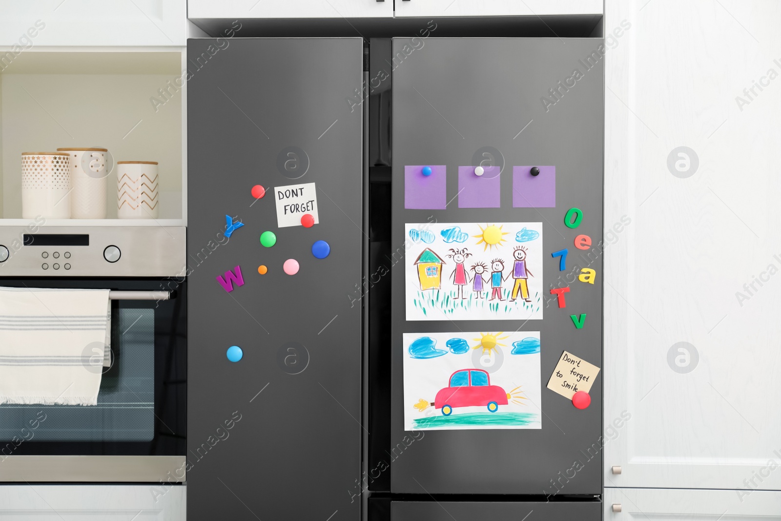 Photo of Modern refrigerator with child's drawings, notes and magnets in kitchen