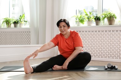 Photo of Overweight mature woman stretching on floor at home