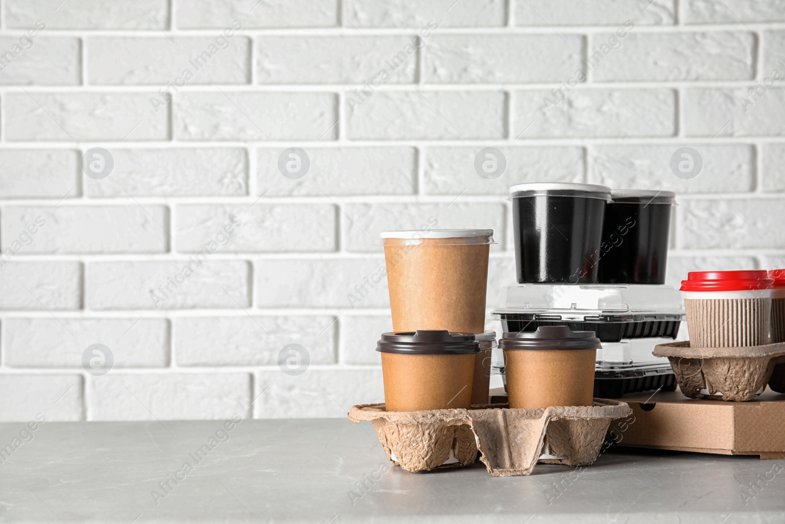 Photo of Various takeout containers on table against white brick wall, space for text. Food delivery service