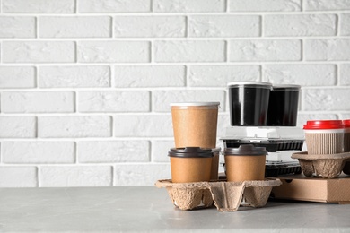 Photo of Various takeout containers on table against white brick wall, space for text. Food delivery service