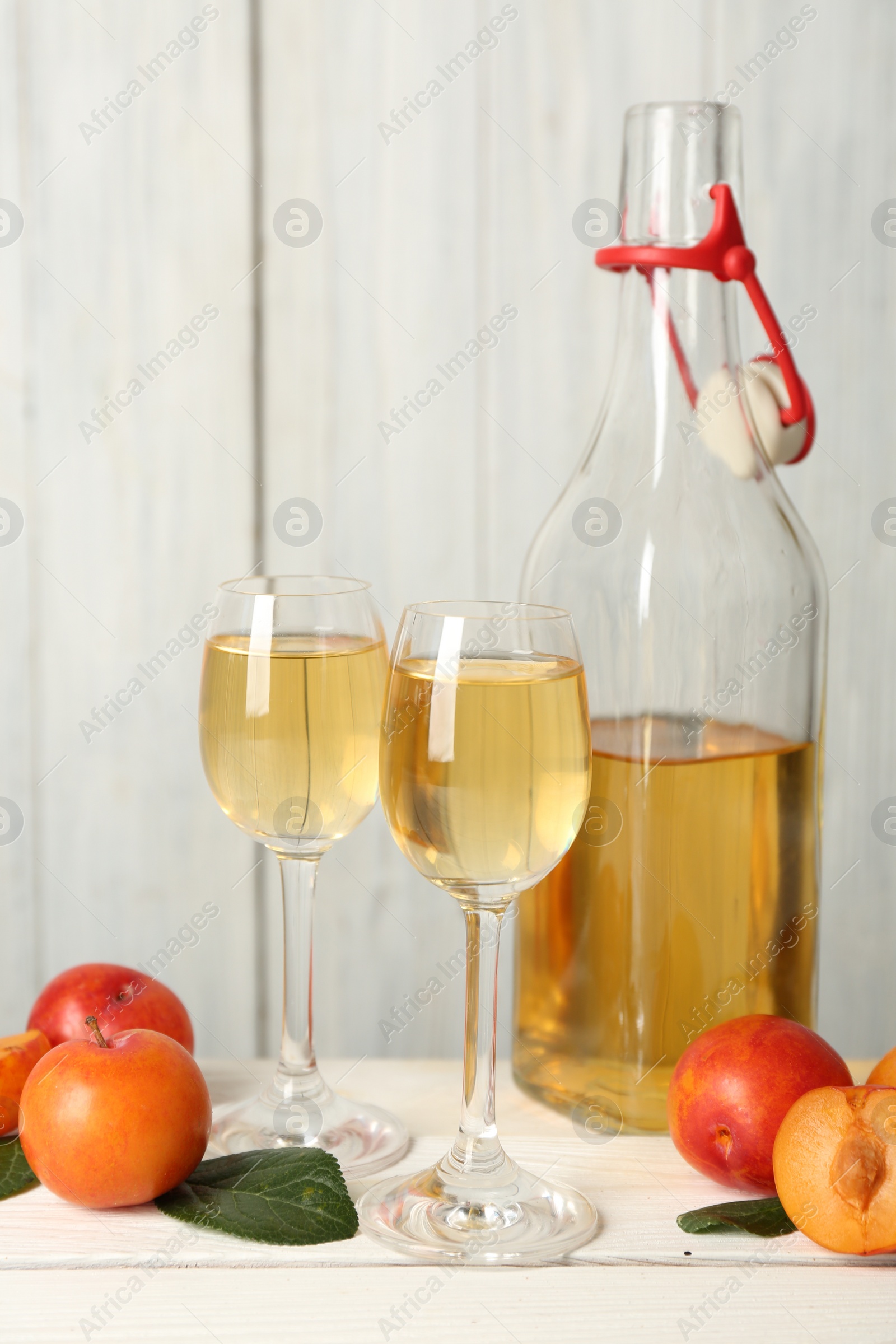 Photo of Delicious plum liquor and ripe fruits on white wooden table. Homemade strong alcoholic beverage