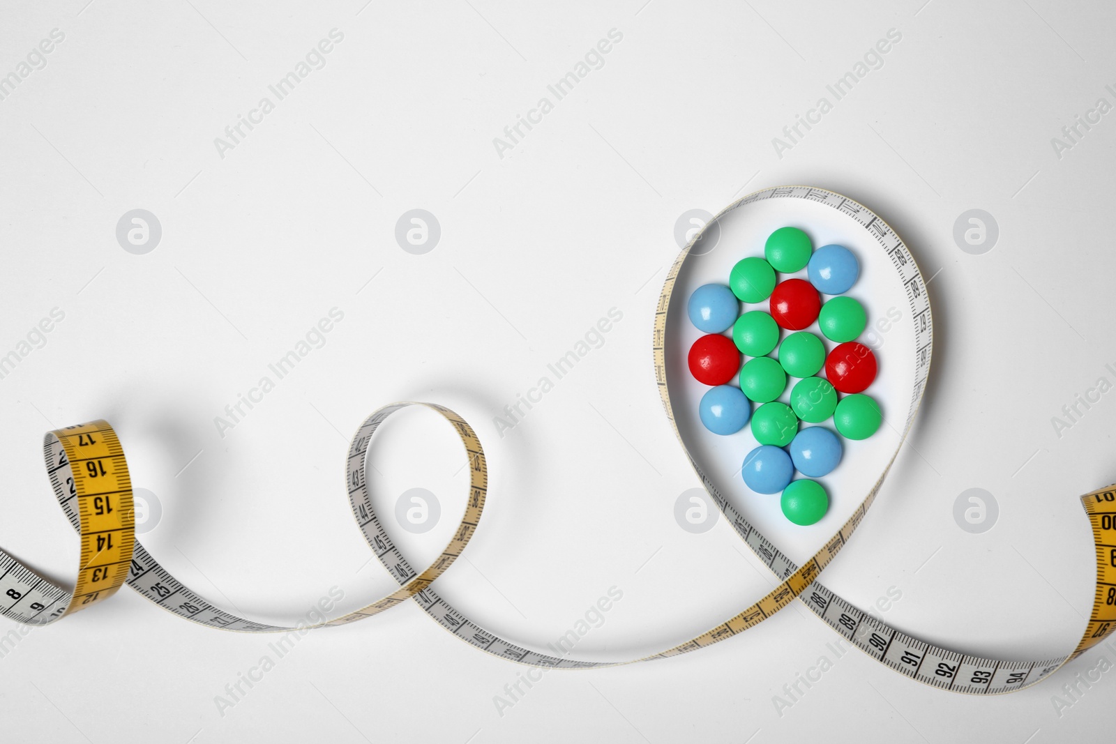 Photo of Weight loss pills and measuring tape on white background, top view