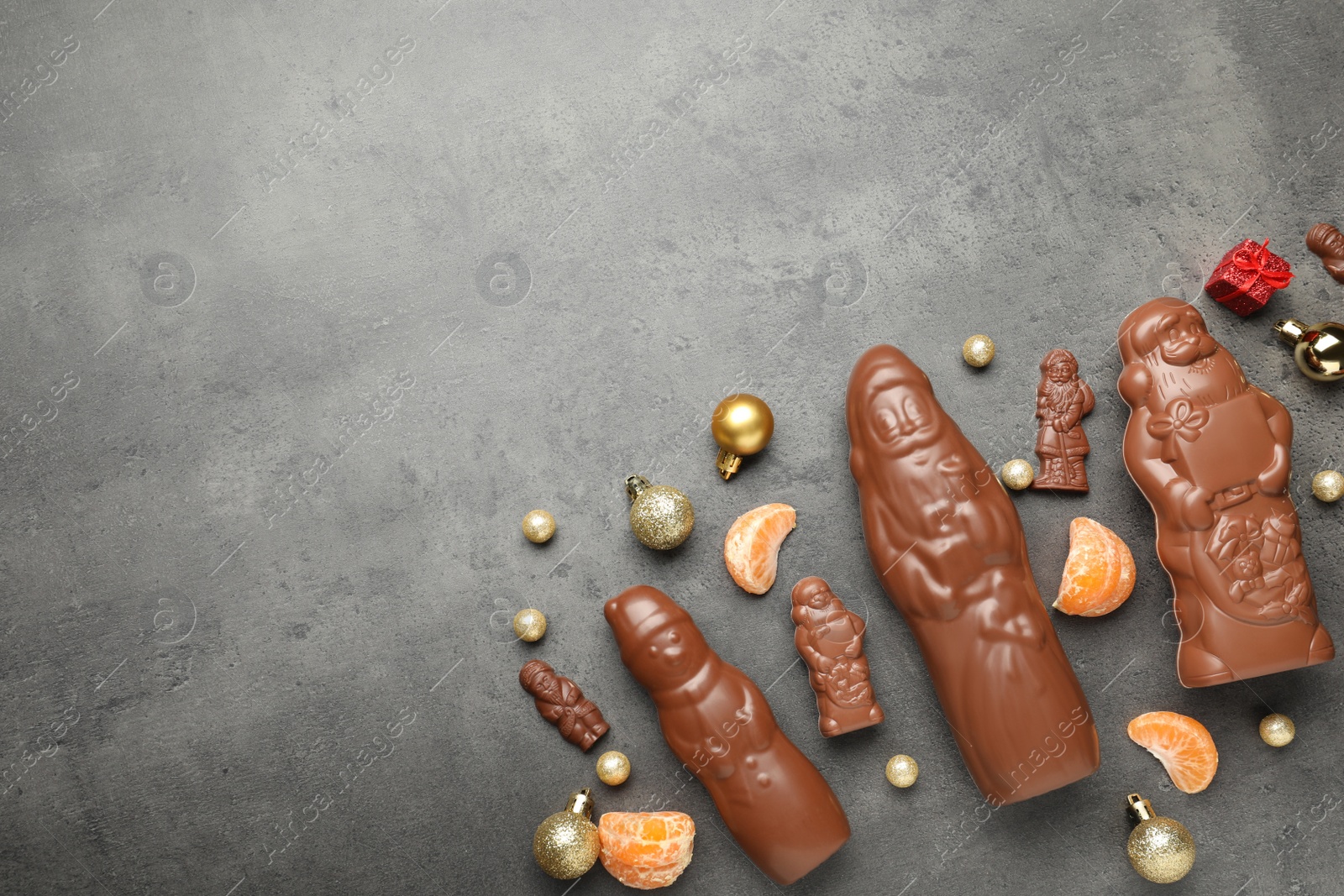 Photo of Flat lay composition with chocolate Santa Claus candies on grey table, space for text