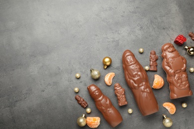 Flat lay composition with chocolate Santa Claus candies on grey table, space for text