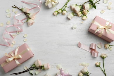 Photo of Flat lay composition with beautiful roses and gift boxes on wooden background. Space for text