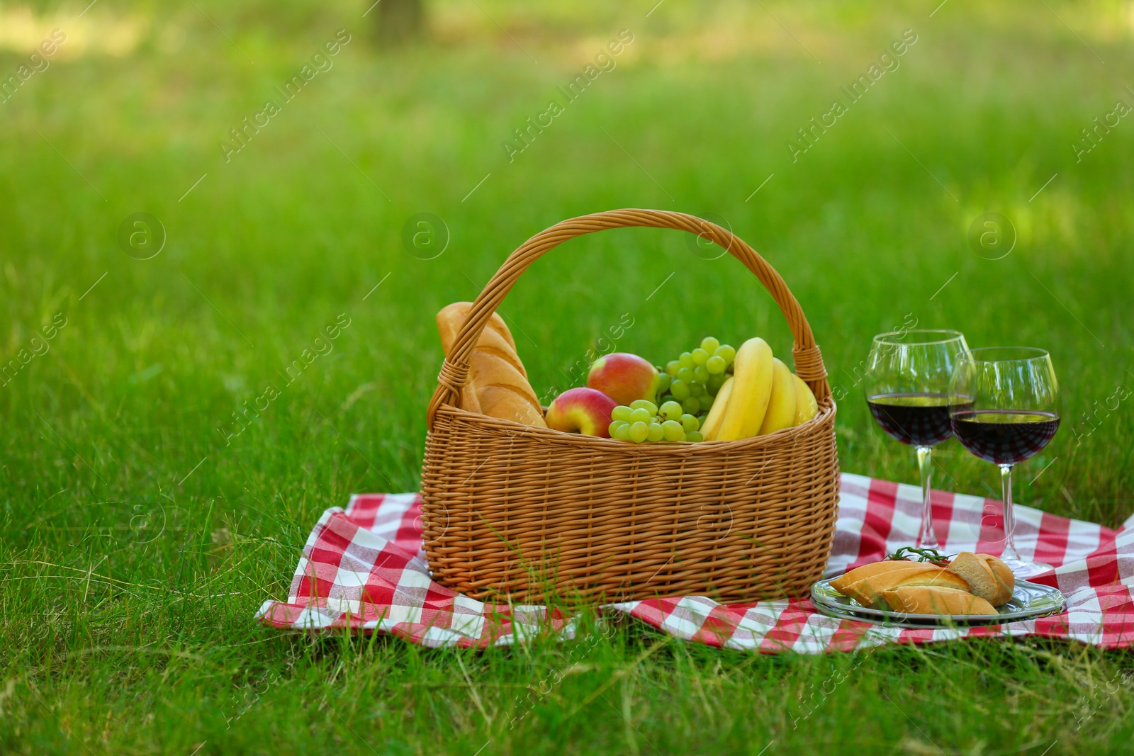 Photo of Wicker basket with food and wine on blanket in park, space for text. Summer picnic