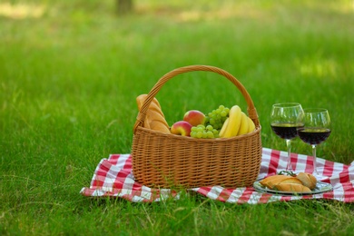 Wicker basket with food and wine on blanket in park, space for text. Summer picnic
