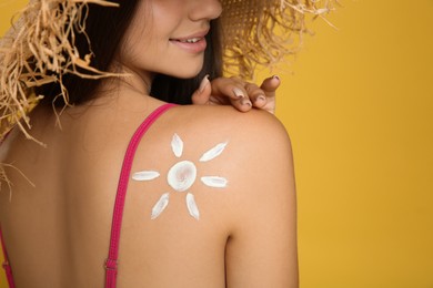 Photo of Teenage girl with sun protection cream on her back against yellow background, closeup
