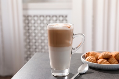 Glass cup of caramel macchiato and tasty pastry on table