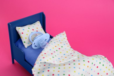 Photo of Maternity leave concept. Toy bed with baby pacifier on pink background
