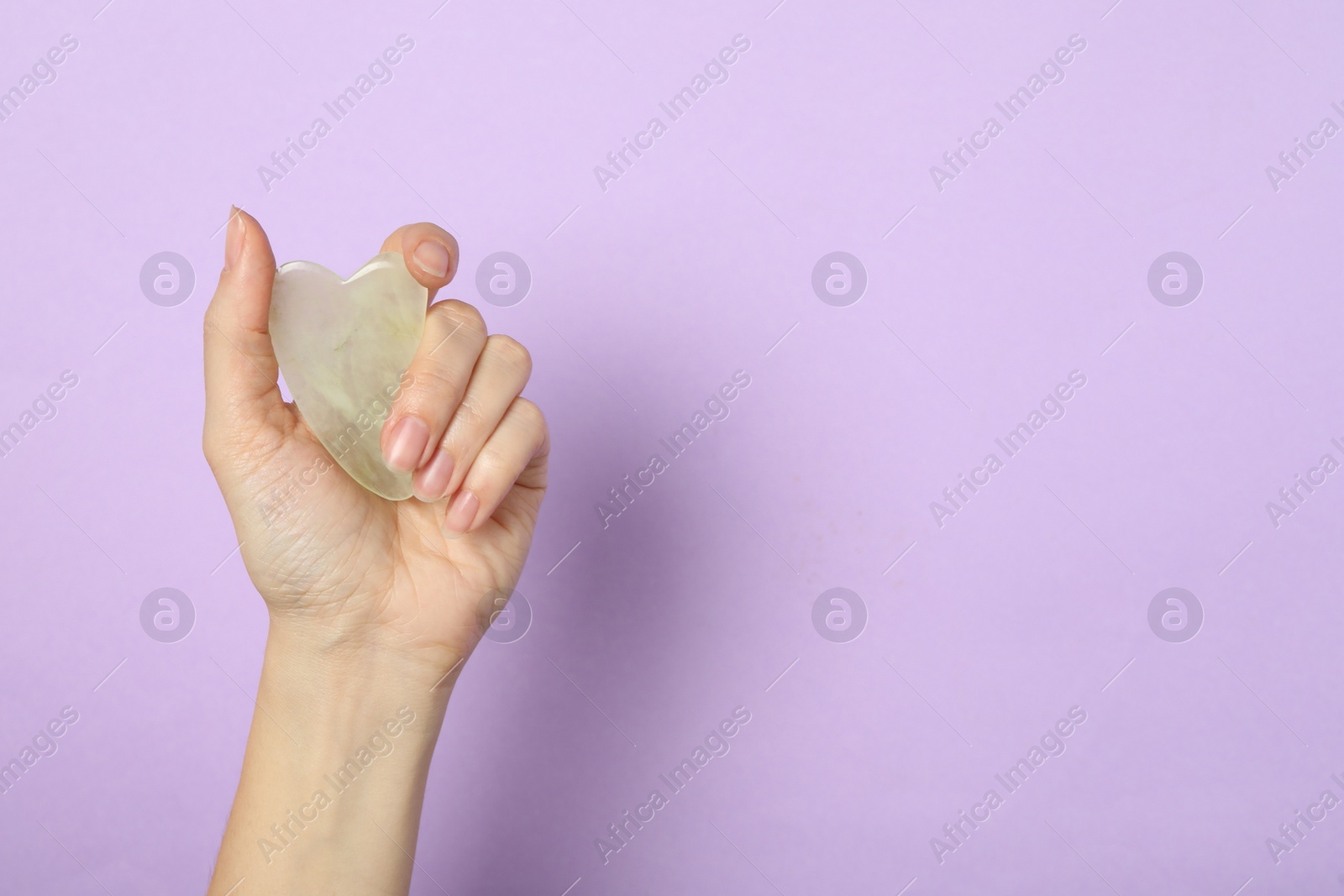 Photo of Woman with jade gua sha tool on lilac background, closeup. Space for text