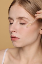 Photo of Woman applying essential oil onto face on beige background