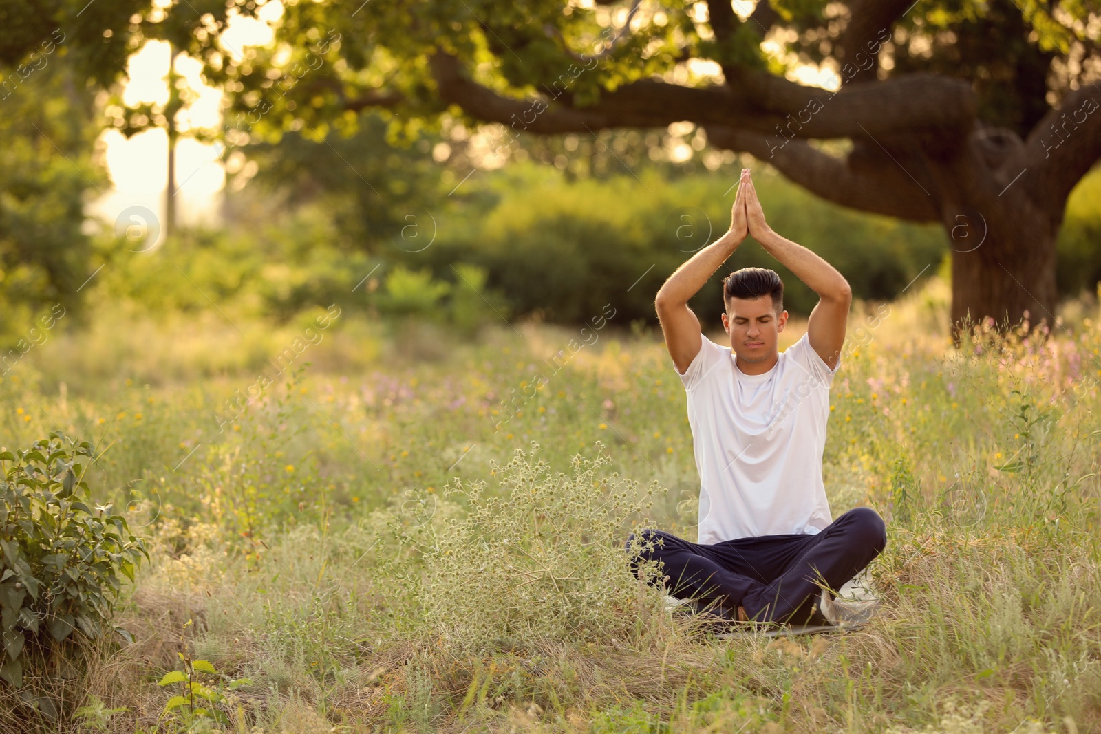 Photo of Man meditating on green grass in park, space for text