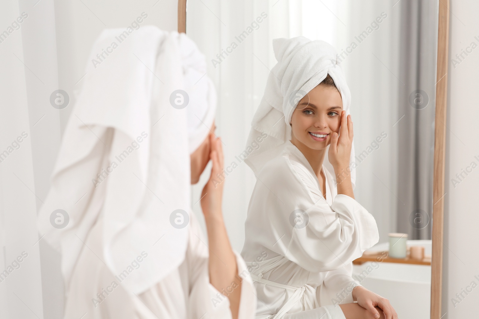 Photo of Beautiful happy woman in white robe near mirror in bathroom