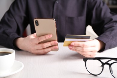 Photo of Online payment. Woman with smartphone and credit card at white wooden table, closeup