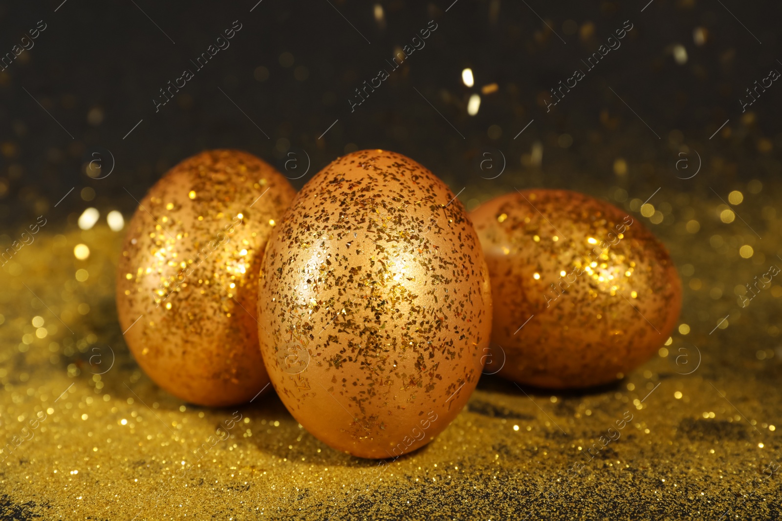 Photo of Shiny golden eggs with glitter on dark table, closeup