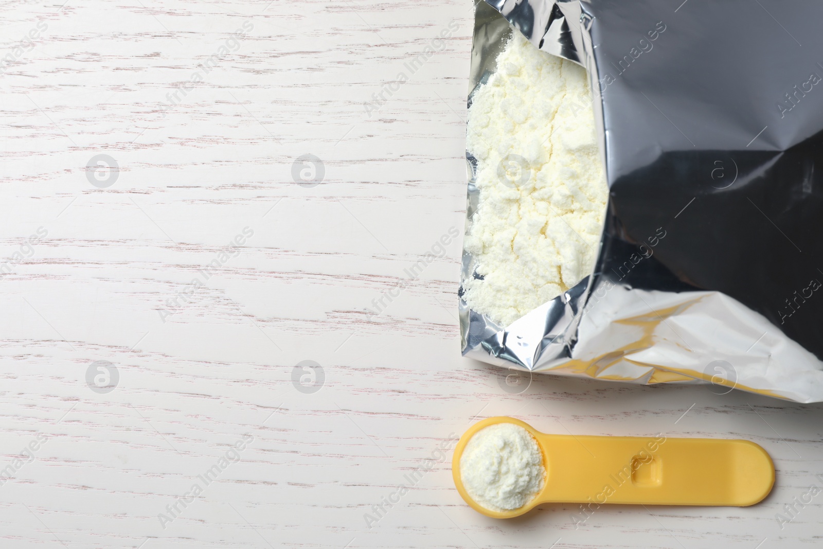 Photo of Bag of powdered infant formula, scoop and space for text on white wooden table, flat lay. Baby milk