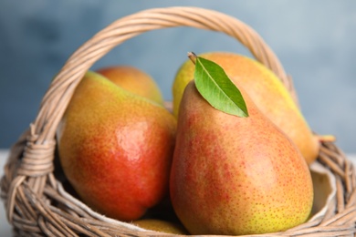 Photo of Ripe juicy pears in wicker basket against blue background, closeup