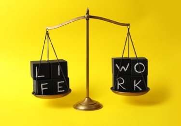 Photo of Words Life, Work made with black cubes on scales against yellow background. Balance concept