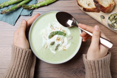 Photo of Woman eating delicious asparagus soup at wooden table, top view