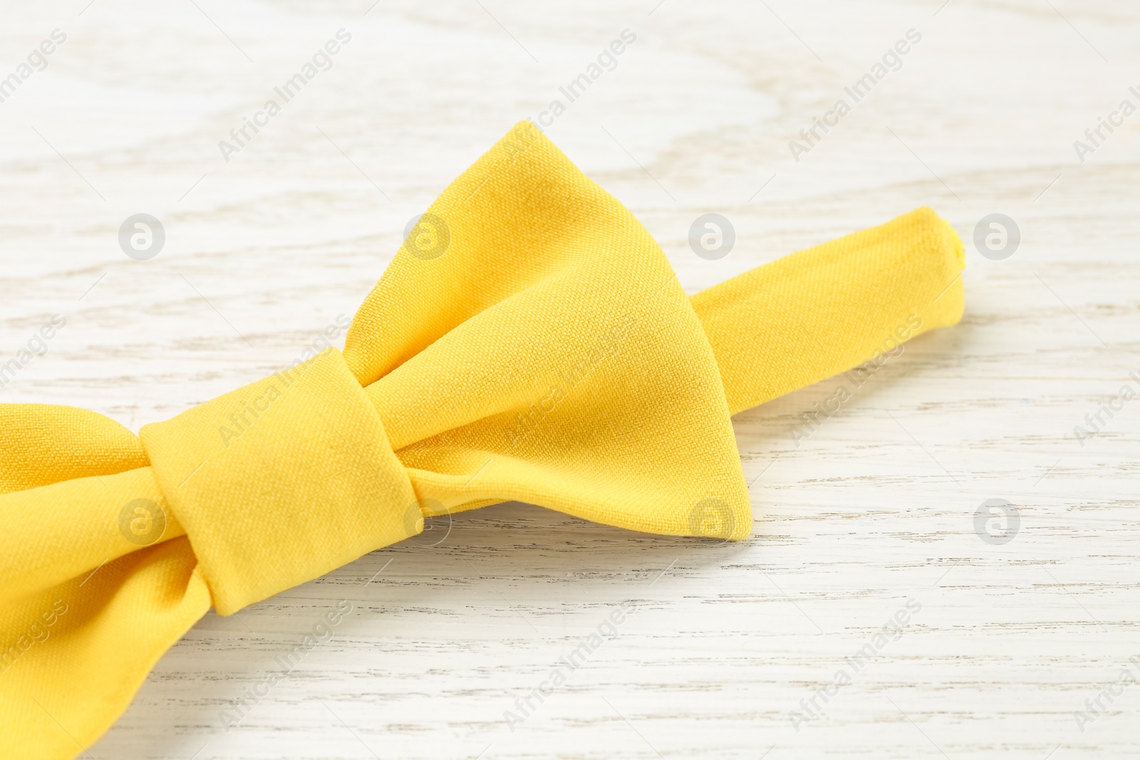 Photo of Stylish yellow bow tie on white wooden background, closeup