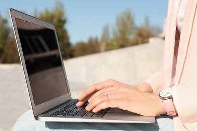 Image of Young woman working on laptop outdoors, closeup