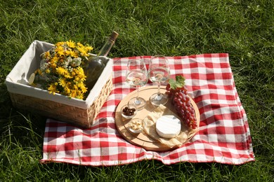 Photo of Glasses of white wine and snacks for picnic served on blanket outdoors