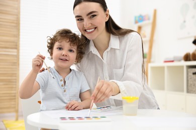 Photo of Mother and her little son painting with watercolor at home