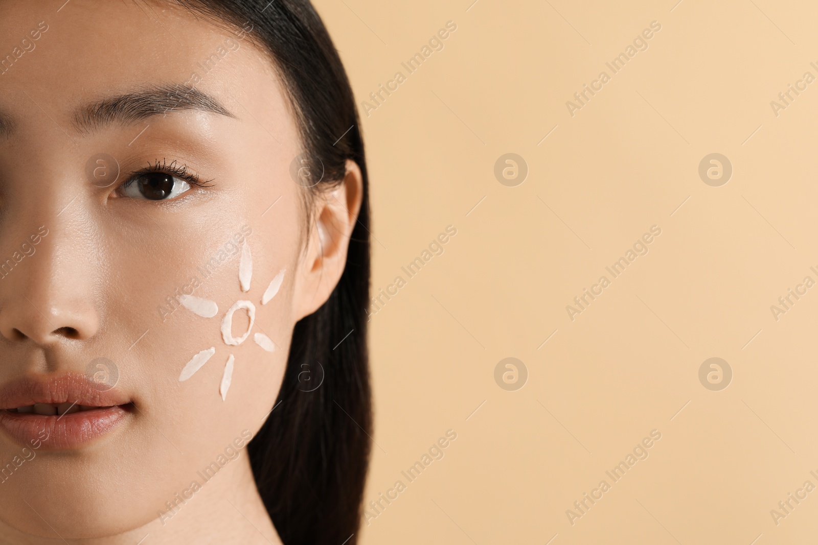 Photo of Beautiful young woman with sun protection cream on her face against beige background, closeup. Space for text