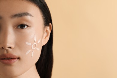 Beautiful young woman with sun protection cream on her face against beige background, closeup. Space for text