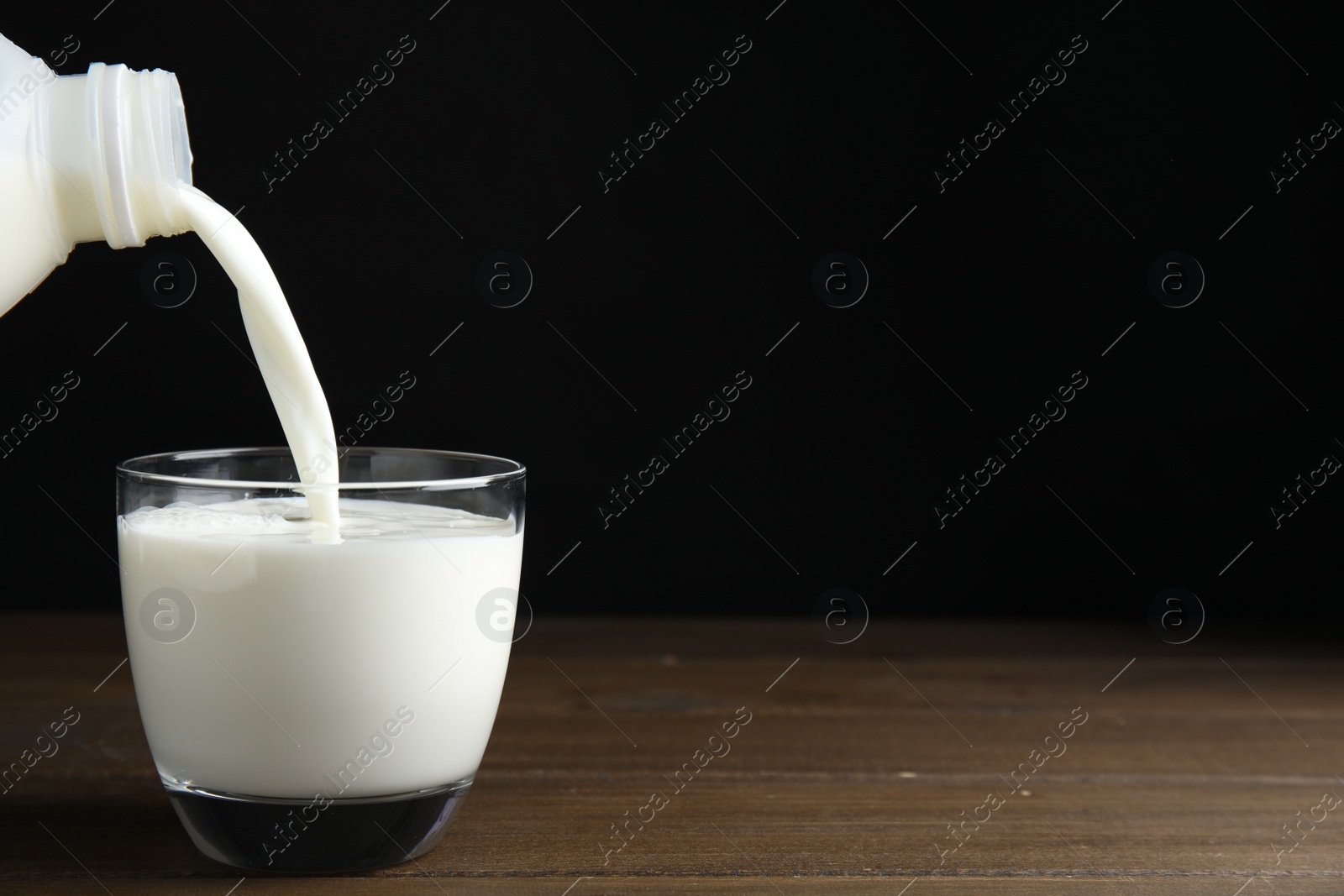 Photo of Pouring milk from gallon bottle into glass on wooden table. Space for text