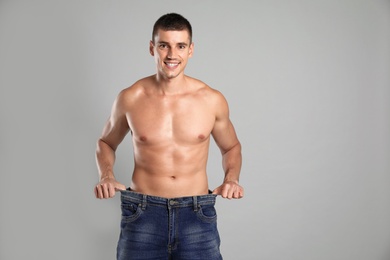 Photo of Young man with slim body in old big size jeans on grey background