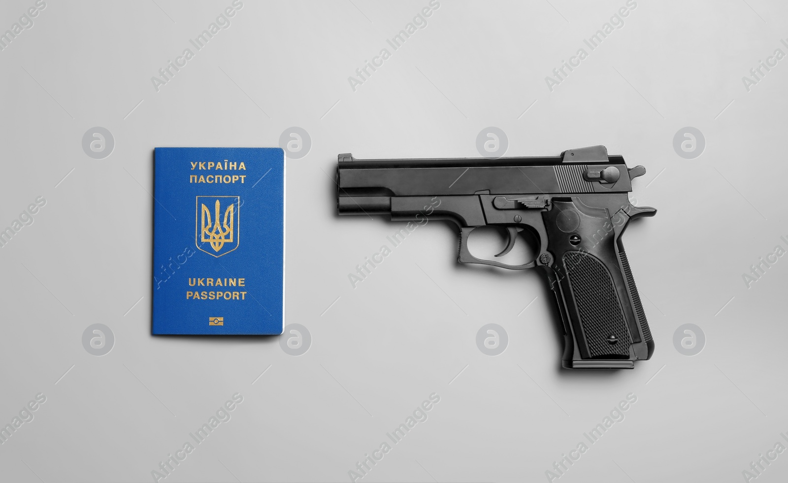 Photo of Gun with Ukrainian travel passport on grey background, flat lay