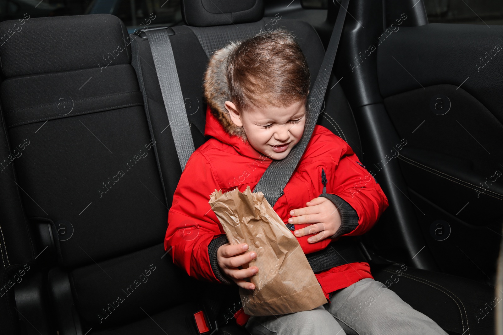 Photo of Little boy with paper bag suffering from nausea in car